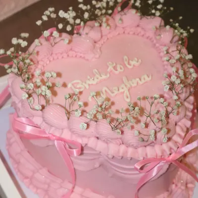 A dreamy, heart-shaped bridal shower cake for a "Bride to be". This all-pink creation features intricate piping, delicate baby's breath flowers, and pretty satin ribbons for a truly romantic feel.