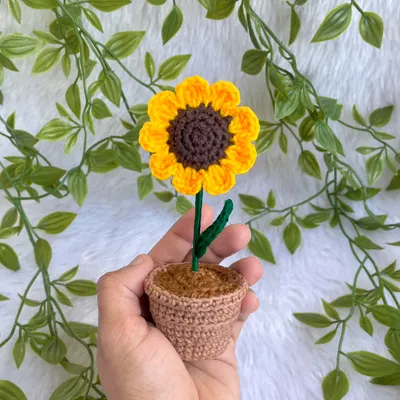 A tiny, adorable potted sunflower held in my hand. This little plant is perfect for adding a touch of handmade charm to any small space.