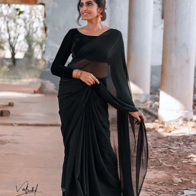 Beauty in simplicity. This full-length shot showcases the graceful drape of a classic black saree. The movement in the fabric and the model's elegant posture create a timeless and sophisticated image.