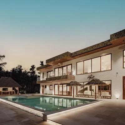 The exterior of Artha Villa at dusk, showcasing its multi-level design, expansive glass windows, and the inviting glow from the poolside, embodying modern tropical architecture.