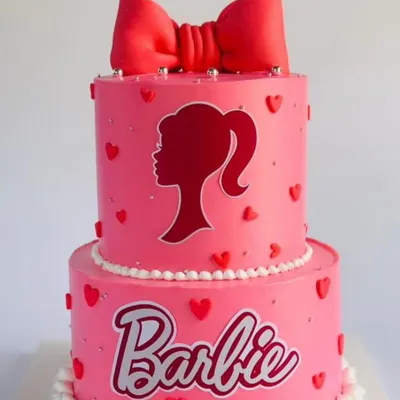 A classic two-tier Barbie cake in pink, featuring the iconic silhouette and a big red bow.