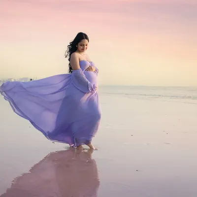Walking on water. The lavender gown flows beautifully as the mother-to-be walks along the shoreline at sunset. The reflection on the wet sand and the pastel sky create a truly magical, painterly effect.