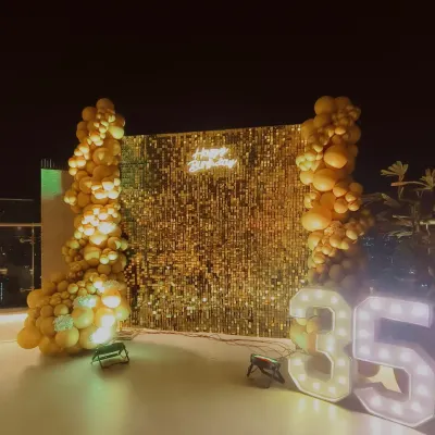 A glamorous 35th birthday setup. The glittering gold sequin wall, 'Happy Birthday' neon sign, and large light-up marquee numbers create a perfect photo spot for celebrating a major milestone.