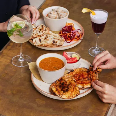 A table full of choices. Creamy chicken malai, rich dal, and flaky parathas paired with a gin and tonic and a deep red sour. This is what a meal at Comorin looks like.