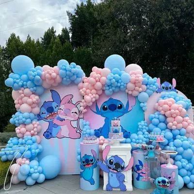 A fun and elaborate birthday party setup based on the popular characters Lilo & Stitch. The decor features large character cutouts, a massive balloon arch in pastel pink and blue, and themed dessert stands.