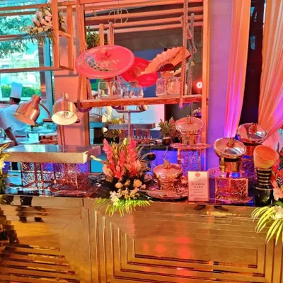 A wide view of our modern buffet setup featuring a geometric gold-mirrored counter. The station is decorated with floral arrangements and uses our signature copper chafing dishes, creating a luxurious look for a wedding.