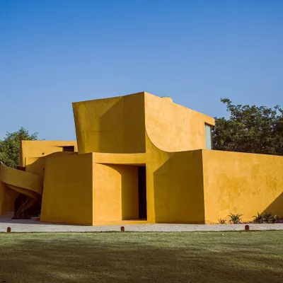 Our main building stands like a sculpture against the clear blue sky, surrounded by lush lawns and trees. The bold yellow and clean lines define the unique architectural character of Anvaya.
