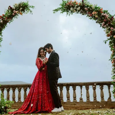 A romantic kiss under a heart-shaped floral arch, set against a serene lake. This is a perfect example of a planned, yet emotionally resonant pre-wedding photograph.