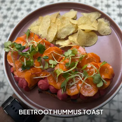 My Beetroot Hummus Toast is a feast for the eyes and the palate. It features creamy, house-made hummus topped with thinly sliced carrots and fresh microgreens on toasted bread.