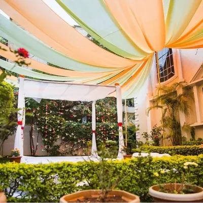 This is an example of an intimate mandap we constructed in a client's backyard. The structure is draped in clean white fabric, while an overhead canopy of pastel green and peach fabric adds a touch of soft color. This setup is perfect for couples looking for a sophisticated and romantic garden ceremony.