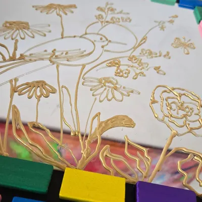 The first step in glass painting is creating a clean, golden outline. This image shows a work in progress, where a delicate design of a bird and flowers is being prepared for vibrant color application.