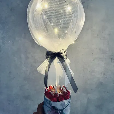 An enchanting balloon hamper featuring a transparent balloon with fairy lights wrapped in tulle, rising from a small floral box of chocolates. A magical gift for under ₹600.