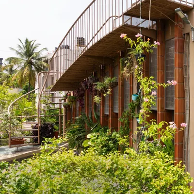 A spiral staircase connects the ground floor garden to the upper terrace, creating a continuous green pathway. The home is wrapped in plants, with creepers and hanging pots that blur the line between the building and the garden.