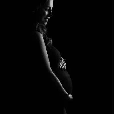 A minimalist masterpiece. This low-key silhouette uses a single stream of light to sculpt the beautiful curve of the baby bump, creating a dramatic and artistic portrait.