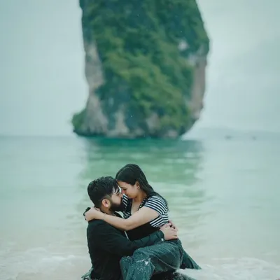 An intimate embrace in the shallow waters of a secluded Thai beach, with a dramatic rock formation in the background.