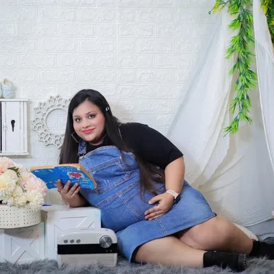 A cozy and casual moment in the studio. The mom-to-be relaxes with a book next to our teepee prop, wearing a comfortable denim overall dress for a relatable and sweet portrait.