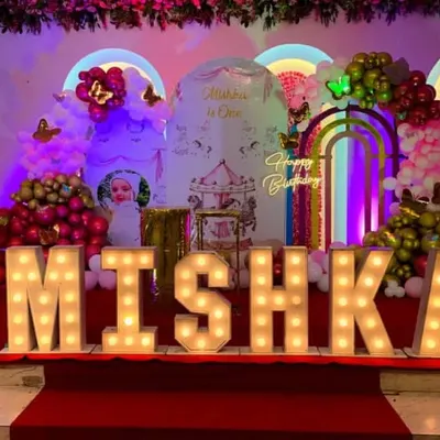 A spectacular first birthday stage for Mishka. This grand setup included large marquee letters spelling her name, a carousel and butterfly-themed backdrop, and multiple balloon arrangements.