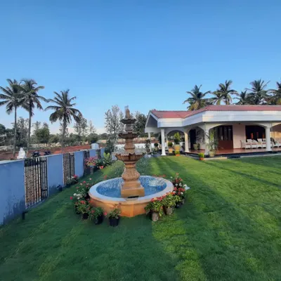 A beautiful farmhouse landscape featuring a classic tiered water fountain as a central element on a lush green lawn. The property is surrounded by coconut palms, creating a luxurious and tranquil setting.