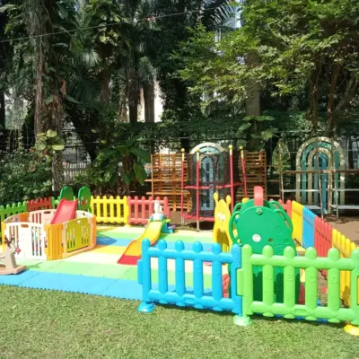 A perfect playzone setup in a lush green garden. This arrangement features multiple slides, climbers, and a rocking horse, all safely enclosed by colorful fencing on soft matting, allowing kids to enjoy the fresh air while they play.