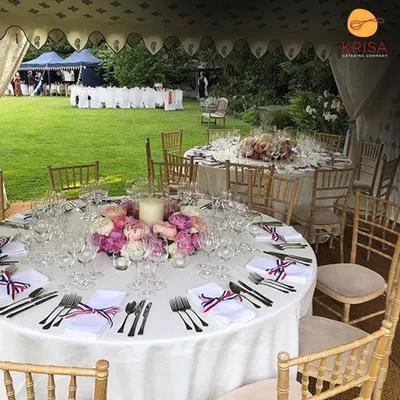 A stunning outdoor sit-down dining setup for a garden party. The round tables are elegantly dressed with white linens, floral centerpieces, and perfectly placed cutlery, creating a sophisticated and welcoming atmosphere for guests.