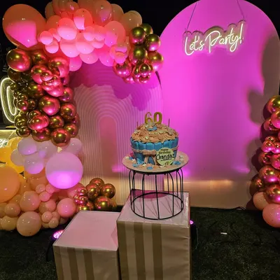 We had the honor of decorating for a 60th birthday party with this vibrant setup. It features a lush balloon arch in shades of pink and chrome gold, a 'Let's Party' neon sign, and a dedicated pedestal to showcase the beautiful birthday cake.