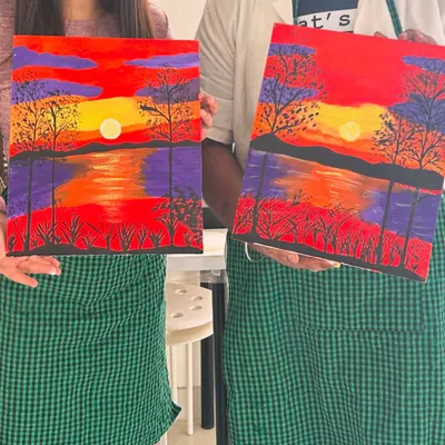 A couple proudly holding their matching sunset paintings. Our guided canvas painting workshops are perfect for beginners and make for a memorable date.