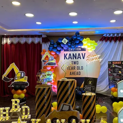 A fun and busy construction theme for a two-year-old. The setup includes caution-striped plinths, excavator cutouts, a personalized 'Caution' sign, and a yellow and black balloon arch.