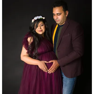 A classic studio portrait of a couple celebrating their growing family. The simple dark background and professional lighting ensure the focus is entirely on their joy and connection.