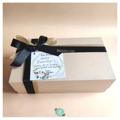 A beautifully wrapped birthday hamper. The simple, elegant box is tied with a black satin ribbon and features a handwritten note, ready to create that "wow" moment.