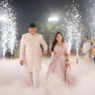 A grand entrance for a beautiful couple. The bride's reception makeup was designed to be luminous and elegant, complementing her sparkling lavender lehenga for a truly magical walk among the smoke and sparklers.