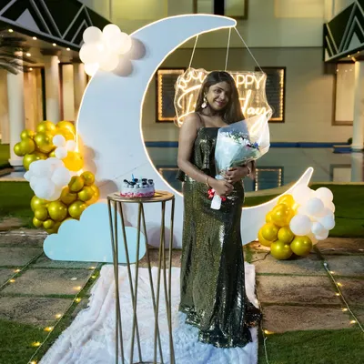 A client posing with our beautiful moon-themed birthday decor. The large crescent moon prop, complete with clouds and a neon sign, creates a dreamy photo opportunity.