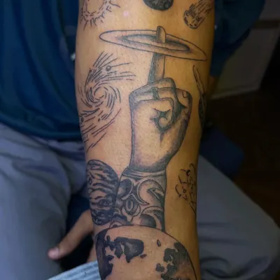 This custom arm sleeve combines various cosmic elements, including planets, a swirling galaxy, and shooting stars. Each element was chosen by the client to build a personal narrative.