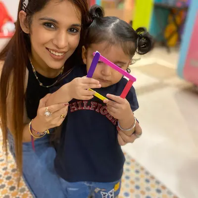 A mother and her child proudly display a shape they created with colorful popsicle sticks. This simple activity helps with learning shapes and colors while strengthening the parent-child bond.