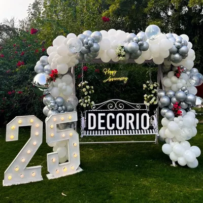 This is the full view of the 25th-anniversary swing setup in a garden. The combination of the balloon arch, neon sign, and large marquee numbers creates a stunning photo opportunity for the celebrating couple and their guests.