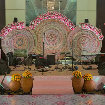 This stage for a Bhaat & Tilak ceremony features large, circular backdrops woven from natural fibers. Paired with fresh pink and white florals, it creates a beautiful fusion of traditional craftsmanship and modern design.