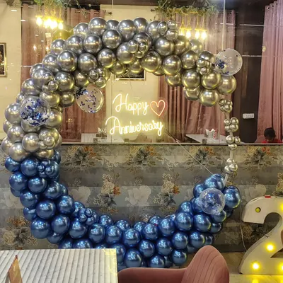 This anniversary backdrop features a stunning balloon ring made of metallic silver and chrome blue balloons. A "Happy Anniversary" neon sign in the center adds a warm glow, making it a perfect photo spot for the happy couple.