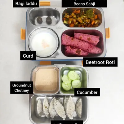 Here's a lunchbox idea with a mix of textures and flavors. It includes millets idly with groundnut chutney, beetroot roti for a colorful twist, a vegetable sabji, cool curd, and a sweet ragi laddu for a healthy treat.