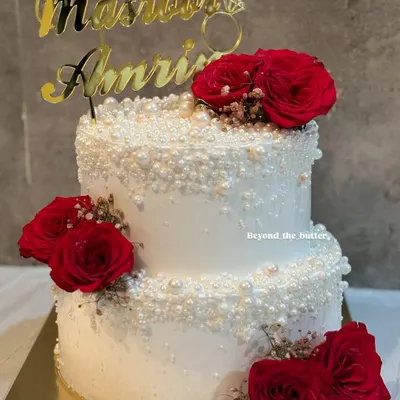 This two-tier wedding cake is the definition of classic romance. I covered it in a cascade of delicate edible pearls and adorned it with clusters of deep red roses and baby's breath, finished with a custom name topper in gold.