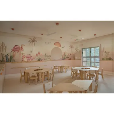 A wide view of the desert-themed Pre-KG classroom, showcasing the expansive wall mural that wraps around the room. The modular, non-plastic tables can be arranged in various formations to support different teaching styles and activities.