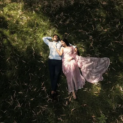 An aerial drone shot captures a quiet moment with the couple resting in a sun-dappled field. This perspective adds a cinematic and peaceful dimension to their pre-wedding story.
