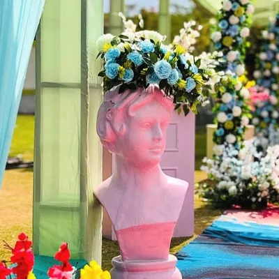 A quirky decor detail featuring a pink bust statue used as a vase for a vibrant blue floral arrangement.