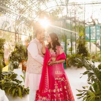 A dreamy, sun-kissed shot of Shree and Abhishek at their Mehendi. Shree is wearing a vibrant pink Anita Dongre lehenga, which looks stunning in the greenhouse setting.