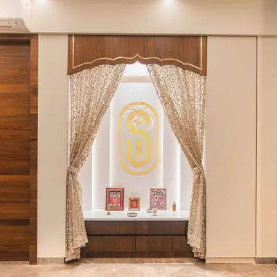 A beautifully crafted pooja unit designed as a serene and sacred space within the home. It features intricate woodwork, elegant curtains, and soft backlighting to create a peaceful ambiance.