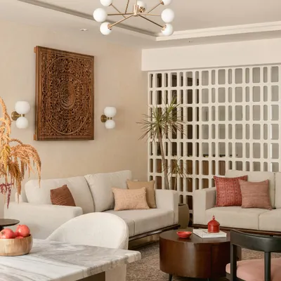 This living room is where modern comfort meets timeless Indian artistry. I anchored the space with a large, hand-carved wooden panel and a delicate jali screen, creating a backdrop that feels both grand and personal. The neutral sofas and contemporary lighting ensure the room remains bright and welcoming, a perfect space for family stories to unfold.