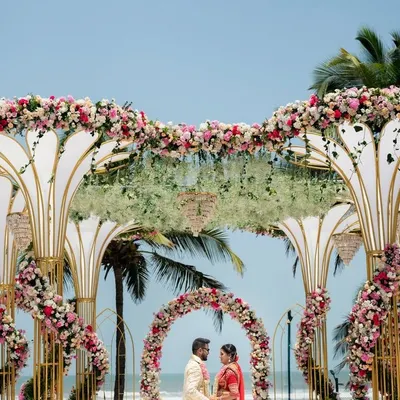 A truly grand mandap for a beach wedding, featuring intricate, large-scale structures adorned with pink and white florals against the ocean backdrop. This design is for couples who want their wedding ceremony to be a statement of pure luxury.