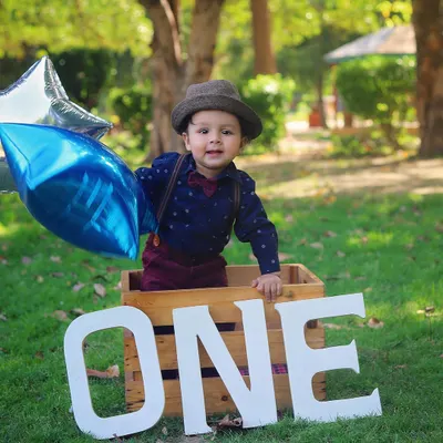 This little gentleman is celebrating his first birthday with an outdoor photoshoot. The natural light and green grass make for a beautiful setting.