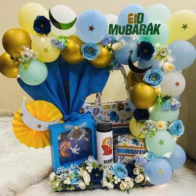 An elegant Eid Mubarak hamper for a little one. This stunning arrangement features a blue and gold theme with balloons, flowers, and personalised gifts like a Tom & Jerry t-shirt and a custom water bottle for 'Hashir'.