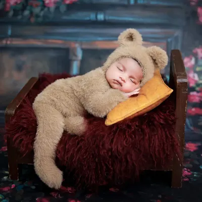 A baby dressed in a fuzzy bear costume sleeps peacefully on a miniature wooden bed. This is one of our most requested adorable prop setups.