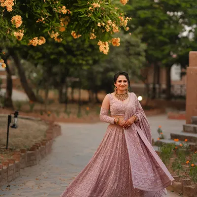 A full-length portrait of the bride, Raman, in her stunning lavender engagement lehenga. The flowering trees at Gaj Resort provide a beautiful, natural frame for this elegant shot.