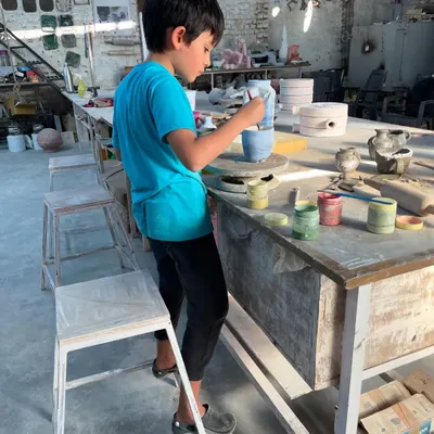 A future potter completely absorbed in his work. He is carefully painting his creation, choosing colors and adding details with intense focus.